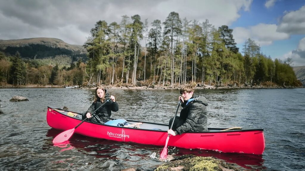 Two people paddling a red canoe on the Great Glen Way in Scotland, surrounded by scenic mountains and calm waters