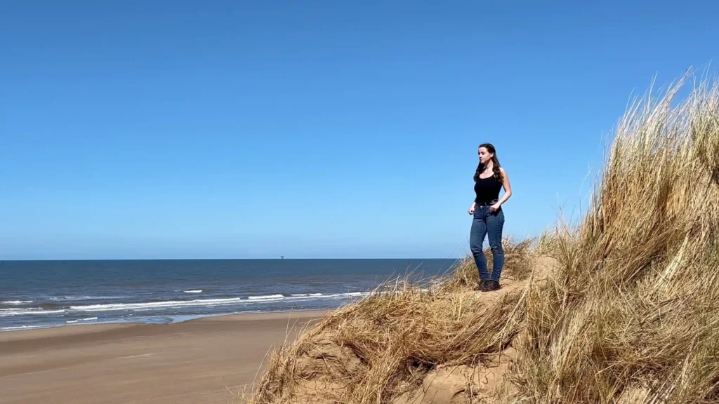 A young girl named Ever Prel standing on top of a sand dune at Formby Beach, Liverpool, looking out at the Irish Sea on a sunny day.