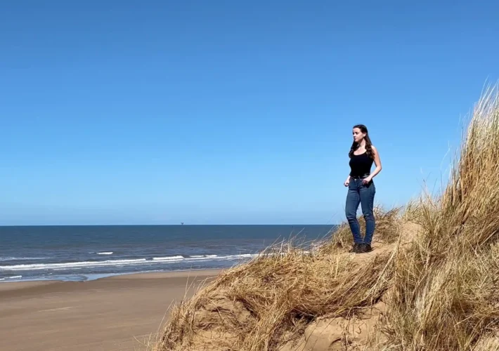 A young girl named Ever Prel standing on top of a sand dune at Formby Beach, Liverpool, looking out at the Irish Sea on a sunny day.