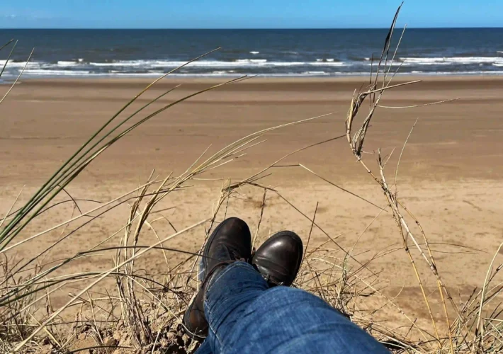 Person sitting on a sand dune at Formby Beach, looking out at the Irish Sea on a sunny day.