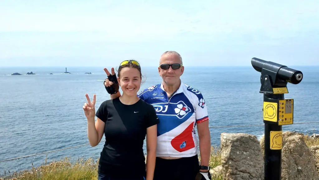 Ever Prel and her dad celebrating their arrival at Land’s End in Cornwall after cycling England's National Cycle Route 2 and 3 on a sunny day with Longships Lighthouse in the background.