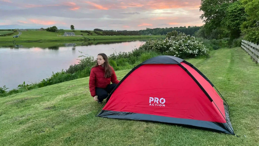 Ever Prel pitching a red tent beside the River Tweed in Scotland at sunset.