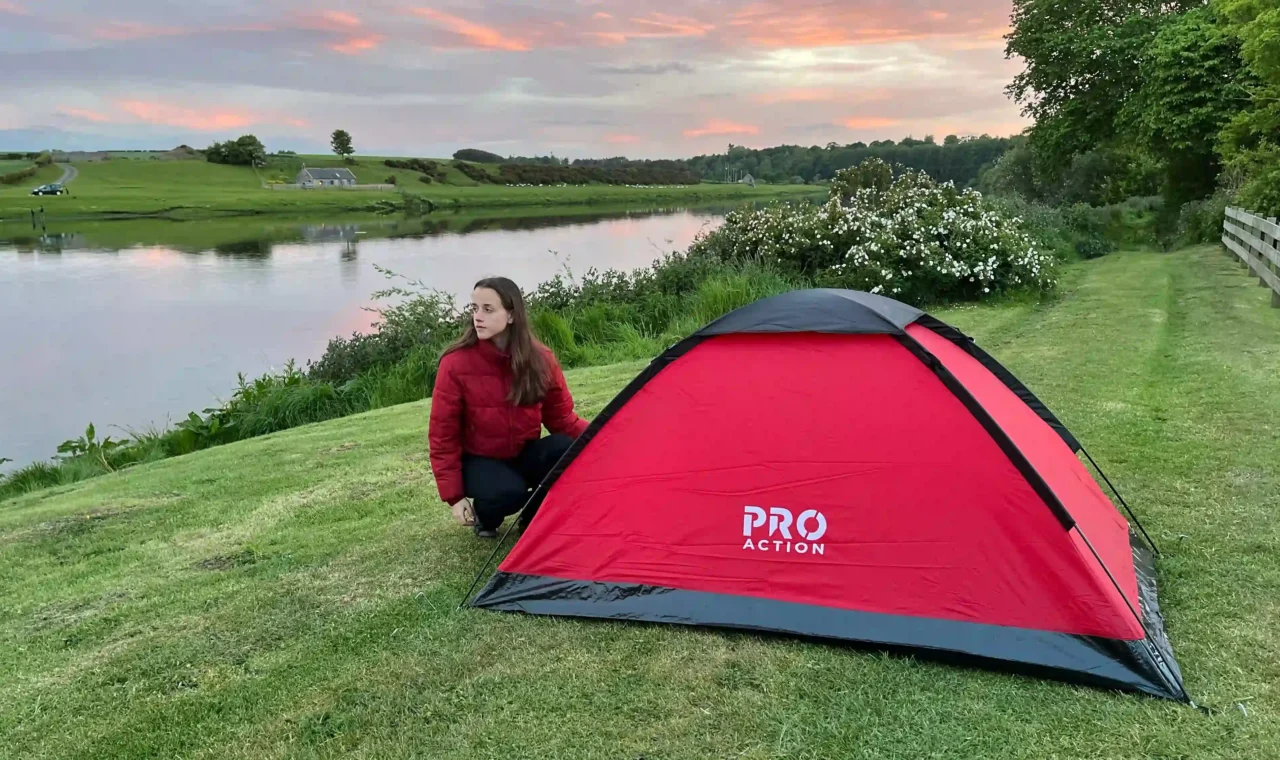 Ever Prel pitching a red tent beside the River Tweed in Scotland at sunset.