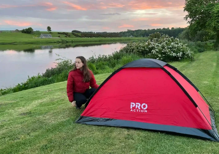 Ever Prel pitching a red tent beside the River Tweed in Scotland at sunset.