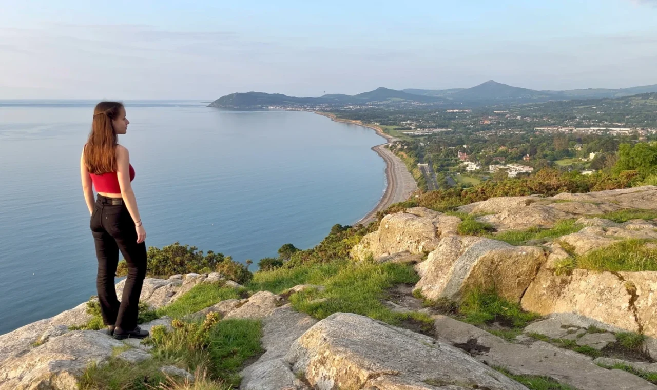 Ever Prel standing on the edge of a cliff on Killiney Hill looking out over Dublin Bay and the Irish Sea