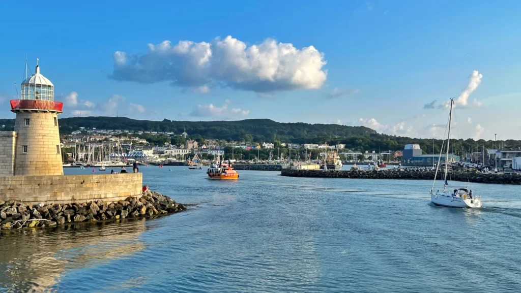 Small boat entering Howth Harbour beside the red and white Howth Lighthouse in Ireland on a sunny afternoon