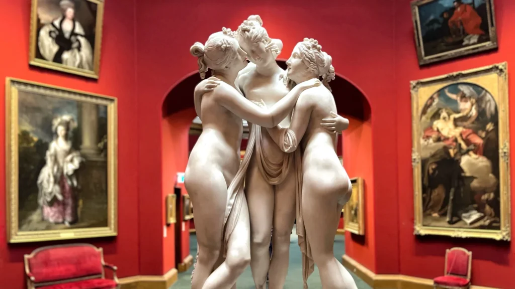 Marble sculpture of the Three Graces surrounded by classical paintings and red walls in the National Galleries of Scotland, one of the must-visit Edinburgh museums.