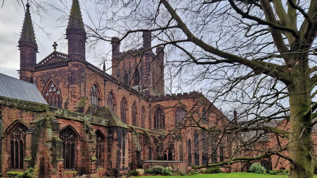 Rear view of Chester Cathedral in Chester, England, seen from the eastern city walls, featuring its red sandstone Gothic architecture, central tower, twin western towers and green lawn in winter.