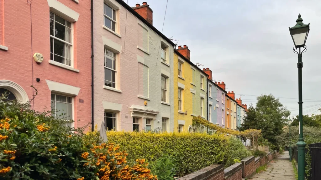 Colourful terraced houses in Nottingham, England, featuring pastel-painted façades, white window frames, traditional brick chimneys and a quiet residential street.