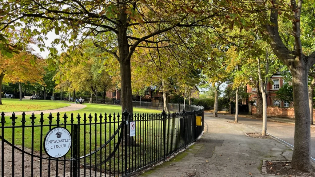 Newcastle Circus garden in Nottingham, England, featuring ornamental black railings, autumn trees, manicured lawns and a peaceful Victorian park setting.