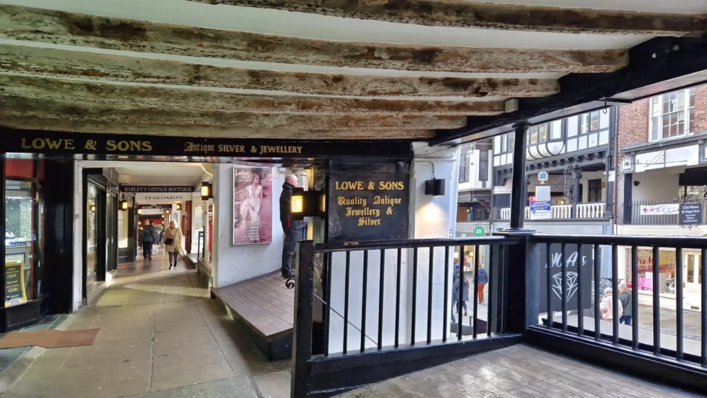 The Chester Rows in Chester, England, featuring the historic covered first-floor shopping galleries with dark timber beams, wooden balustrades, Christmas decorations and views over the cobbled street below.