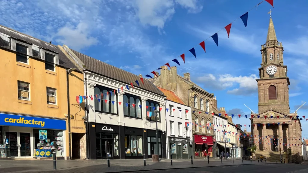 Berwick-upon-Tweed town centre high street with shops, bunting and the clock tower against a blue sky