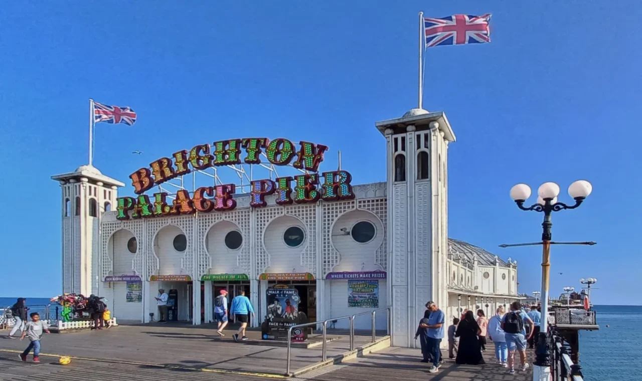 Entrance to Brighton Palace Pier with colourful sign and Union Jack flags flying under a blue sky