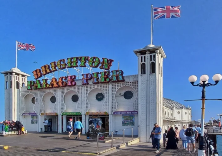 Entrance to Brighton Palace Pier with colourful sign and Union Jack flags flying under a blue sky