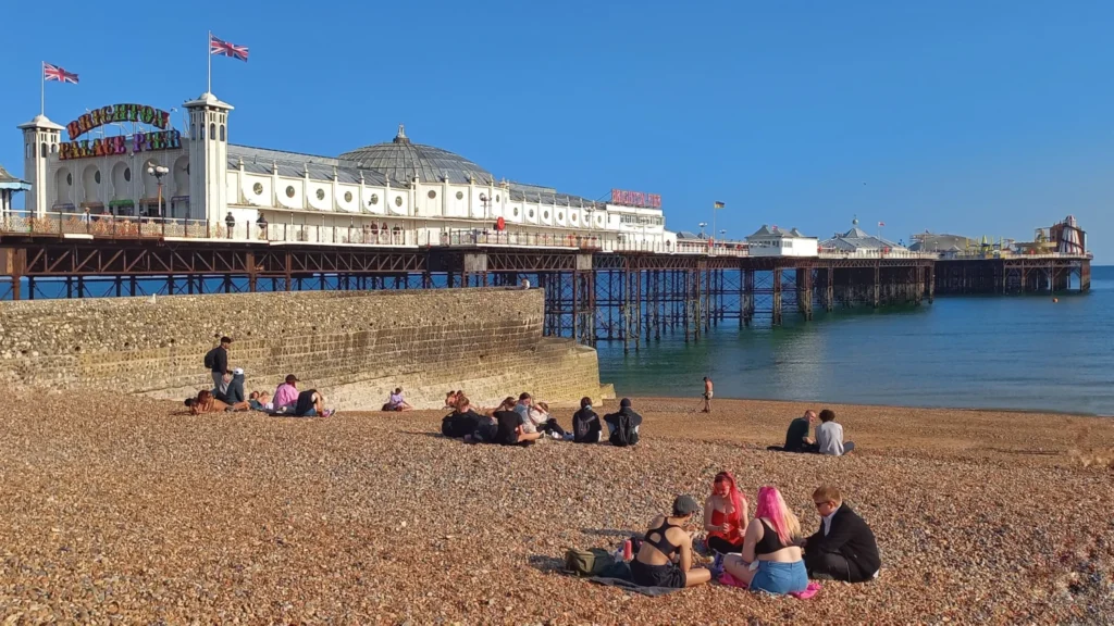 Brighton Palace Pier viewed from the pebble beach with visitors relaxing in the sun