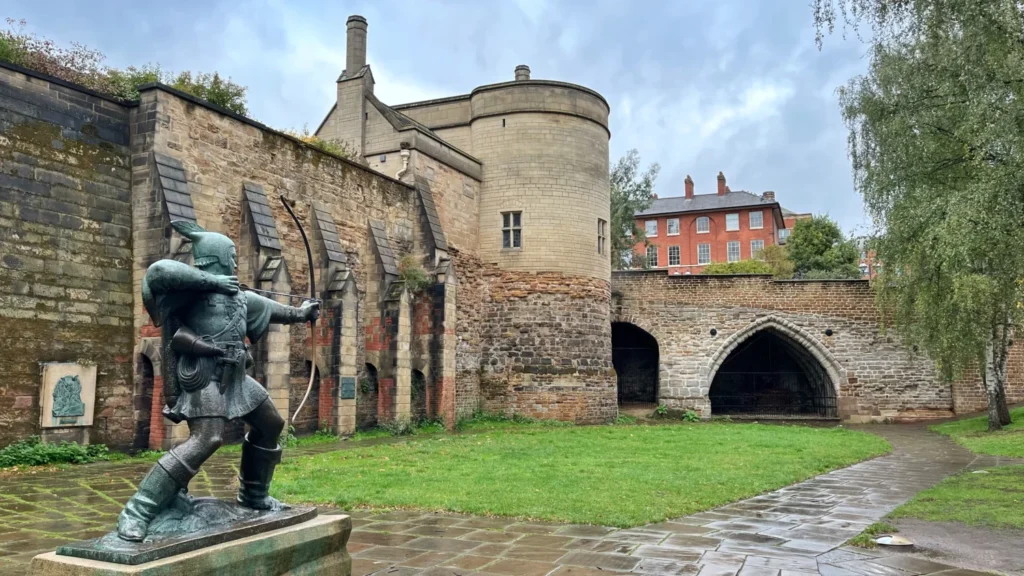 Robin Hood statue with bow drawn in front of Nottingham Castle's medieval gatehouse walls