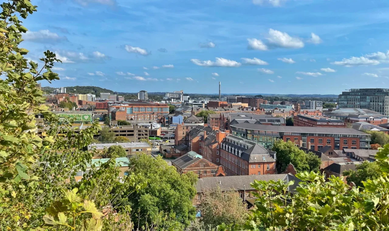 Panoramic view over Nottingham's rooftops and skyline seen from Nottingham Castle, framed by green trees