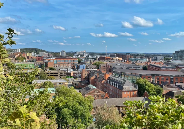 Panoramic view over Nottingham's rooftops and skyline seen from Nottingham Castle, framed by green trees