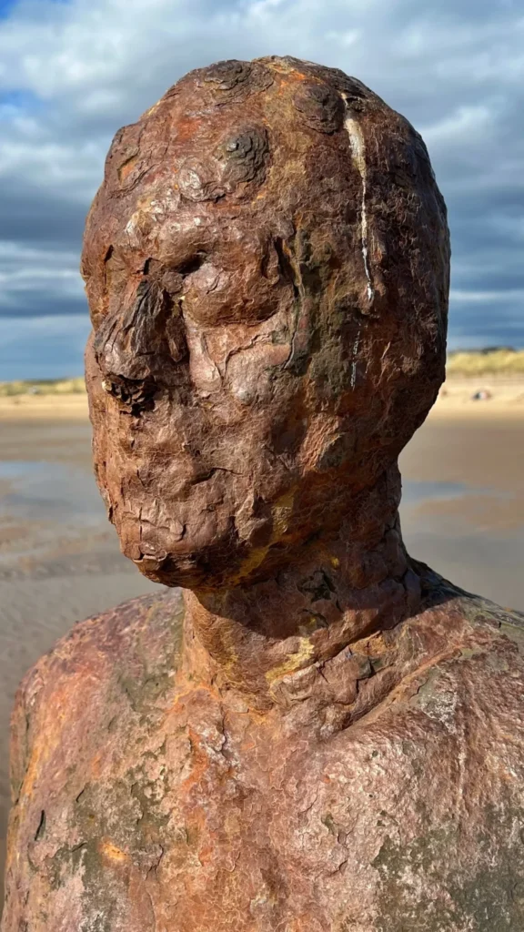 Close-up of a rusted cast-iron figure from Antony Gormley's Another Place, weathered by sea and sand at Crosby Beach