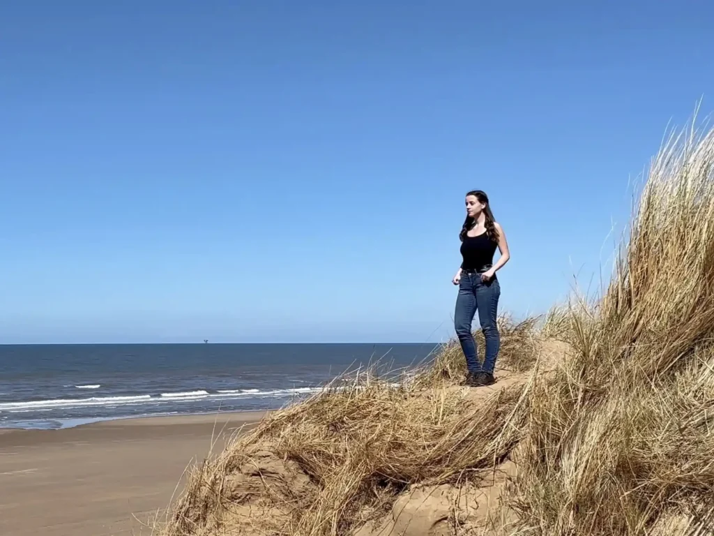Woman standing on the sand dunes at Formby Beach, surrounded by marram grass, looking out over the sea