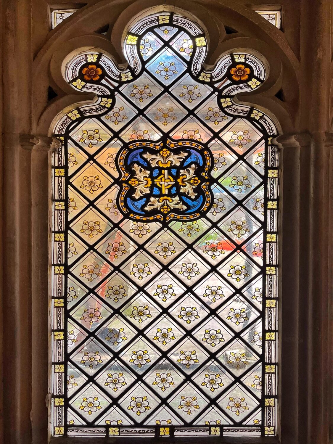 A diamond-quarry stained glass window in the cloisters at Gloucester Cathedral, with a painted cross at its centre