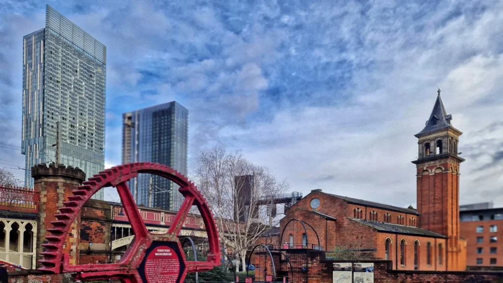 Manchester skyscrapers rising above the red brick Grocers Warehouse and a historic gear wheel monument by the canal