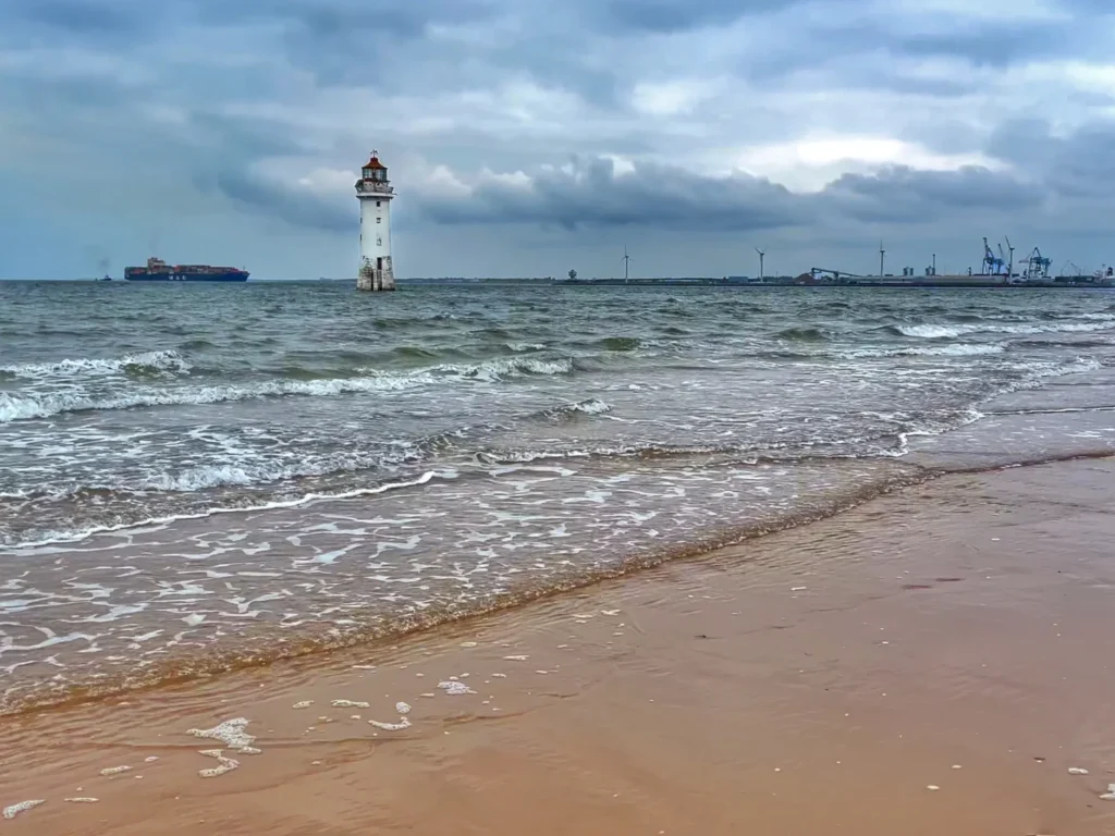 Perch Rock Lighthouse standing in the sea off New Brighton, with a container ship and dockside cranes in the background