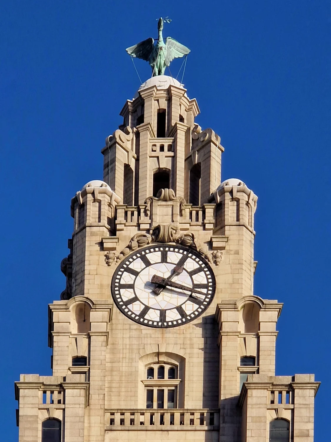 Close-up of the Royal Liver Building's clock tower with a bronze Liver Bird statue against a clear blue sky in Liverpool
