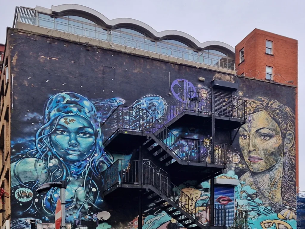 Subism Collective mural on Church Street, Manchester, showing two elemental female figures either side of a fire escape