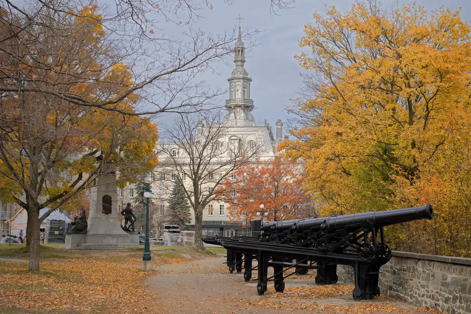Old black cannons along a stone wall under orange fall trees in Québec City